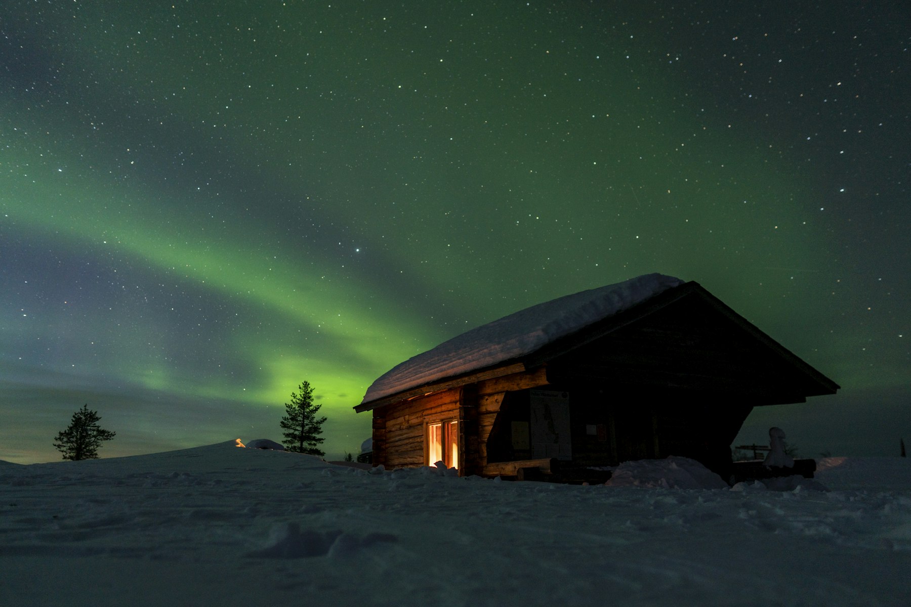 Northern lights glowing over a Scandinavian cabin in the snow